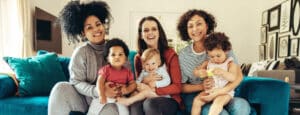 A group of mothers sit on a couch holding their toddlers
