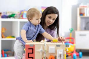 A child care provider helps a toddler play with an interactive toy in a care center