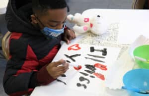 A boy hand paints a sign for his deploying parent during Operation Hero that says "I'll miss you"