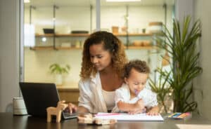 Mom with young child on her lap working on the computer is a reality of how to build a business