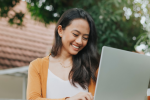 Smiling woman typing on her laptop in an outdoor setting.