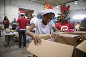 Girls wearing Santa hats are packing supplies in a volunteer center.