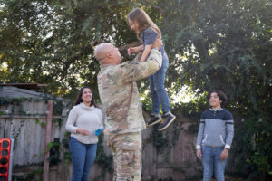 Military service member lifting up his child to the sky while his family looks on