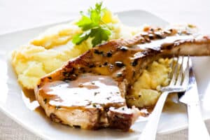 A plate of glazed pork chops with mashed potatoes garnished with parsley.