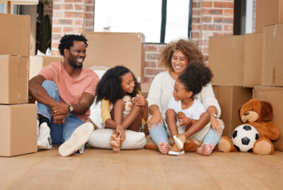 A military family sitting on the floor surrounded by moving boxes, smiling and enjoying a moment during a PCS move.