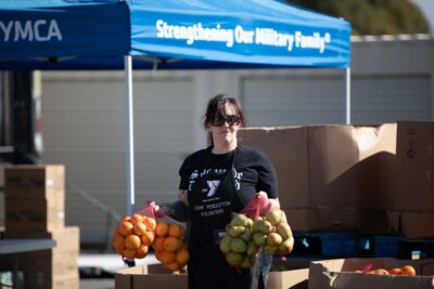ASYMCA volunteer holding fresh fruits at a food distribution event.