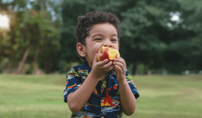 Smiling young boy eating an apple outdoors, symbolizing hope and support in the fight against food insecurity.
