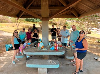 group of people smiling for a photo as they gather around a picnic table outdoors