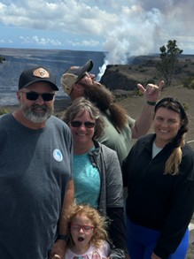 family poses for picture with a volcano venting in the background