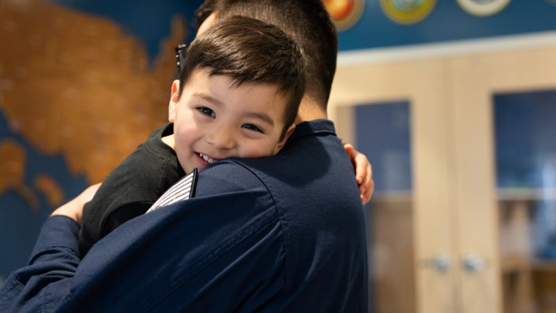 A smiling little boy hugs his navy father goodbye in the lobby of the Norfolk CDC during drop off