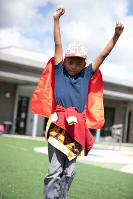 Military kid with cape and hands raised at ASYMCA Operation Hero program