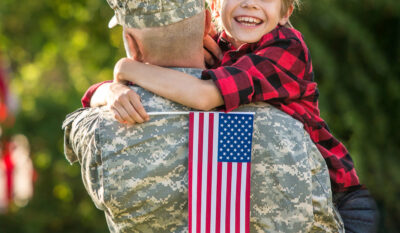 Military service member hugging son holding an American flag
