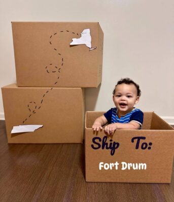 Smiling military child inside a moving box with words Ship to Fort Drum