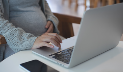 Pregnant military spouse types on laptop in her kitchen