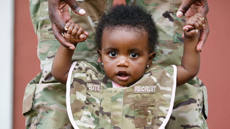 Toddler holding military mother's hands with camo bib that says 