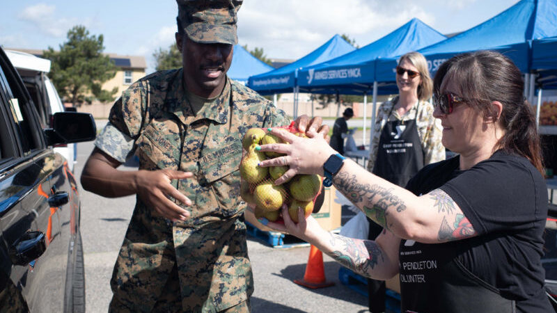 A marine helps an ASYMCA staff member transfer a bag of produce to a vehicle during a food distribution event